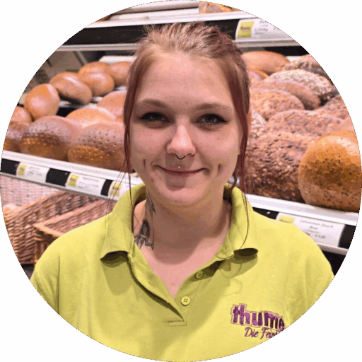 Verkäuferin Frau Lorenz steht freundlich lächelnd hinter der Ladentheke der Feinbäckerei Thume, bereit, Kunden zu bedienen.
